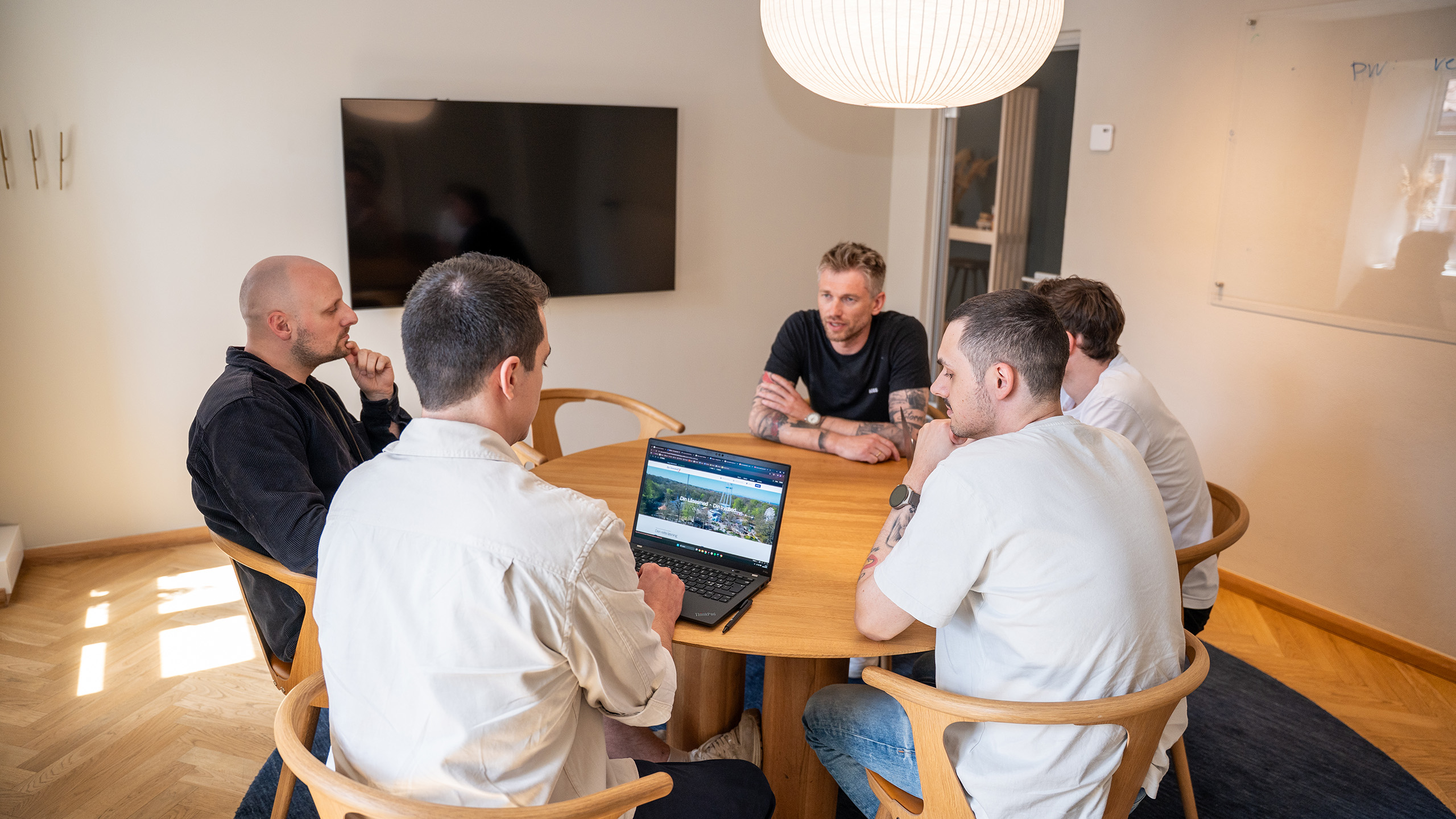 Billede af 5 mandlige ansatte der sidder om et rundt bord i et mødelokale